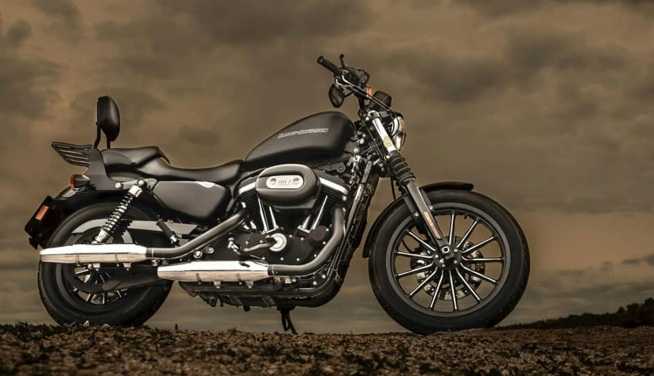 A black cruiser motorcycle parked on a barren landscape with a cloudy sky backdrop