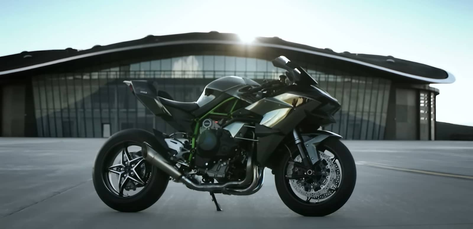 A sleek motorcycle stands in daylight with a modern building behind